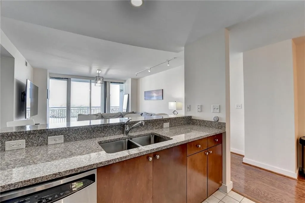 Kitchen with stainless steel dishwasher, light stone countertops, sink, and light hardwood / wood-style flooring