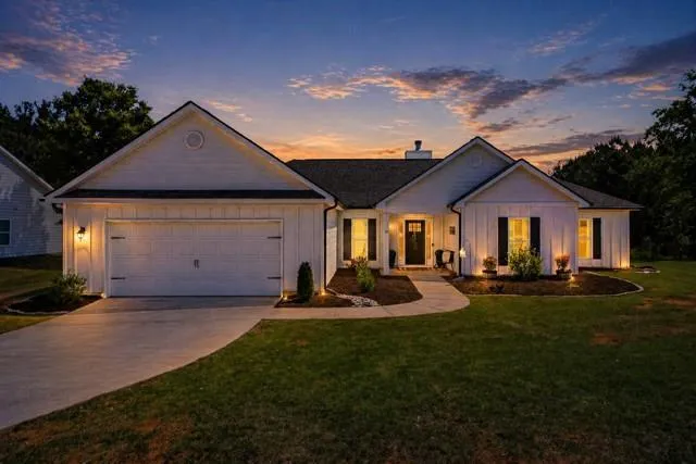 Contemporary ranch exterior featuring white board and batten siding, dark shingle roofing, a concrete driveway, an integrated garage, and a curved paved walkway