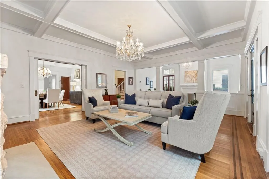 Living area featuring a chandelier, beamed ceiling, coffered ceiling, wood finished floors, and ornamental molding