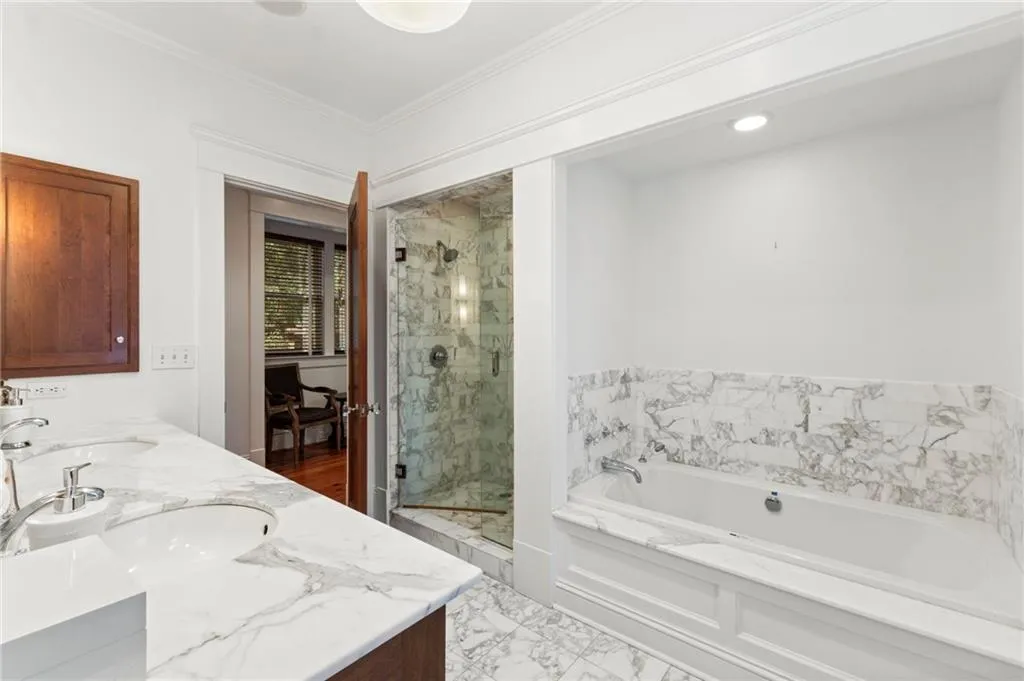 Bathroom featuring a marble finish shower, double vanity, a garden tub, ornamental molding, and light marble finish flooring