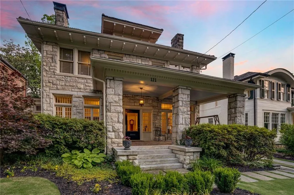 Back of property at dusk featuring stone siding, covered porch, and a chimney