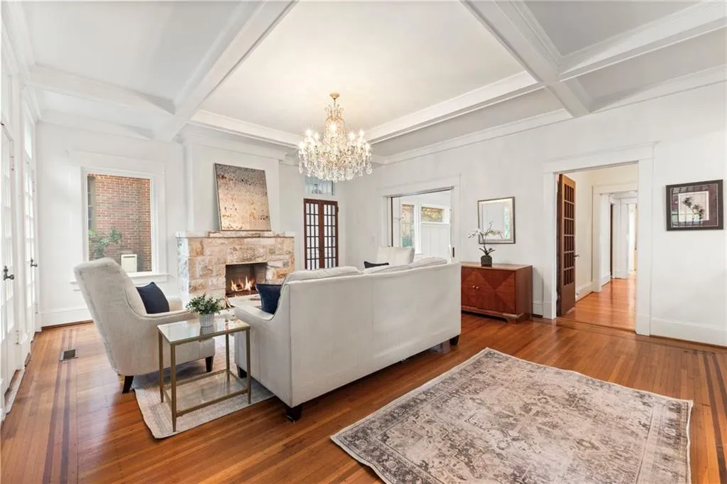 Living room with beam ceiling, hardwood / wood-style floors, coffered ceiling, a fireplace, and a chandelier