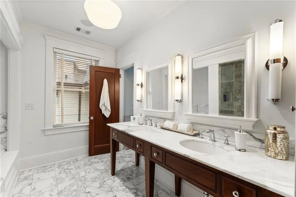 Bathroom featuring light marble finish floors, ornamental molding, and double vanity