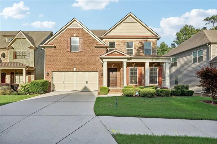 Brick and stone-clad exterior with a prominent front porch, two-car garage, and established landscaping