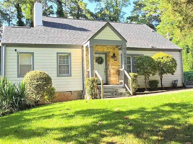 Charming residence featuring a stone-clad portico, a white entry door with a wreath, and a shingled roof