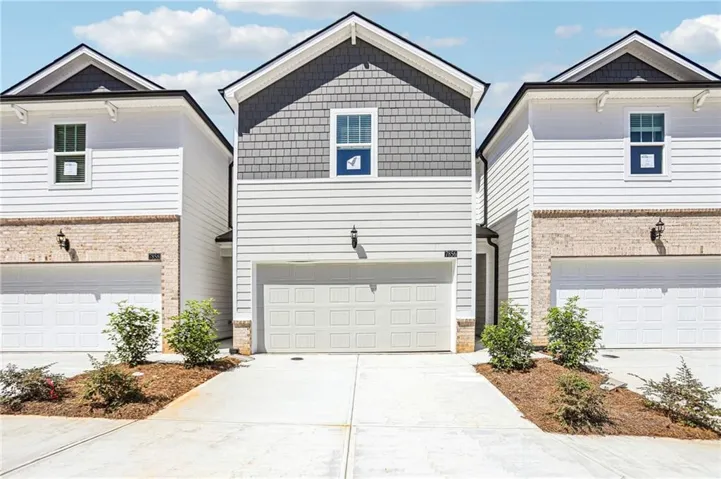 Modern townhome community featuring three coordinated residences with clean-lined architecture, white and gray exterior finishes with mixed siding and stone accents, gabled rooflines with dark trim, and front-load two-car garages
