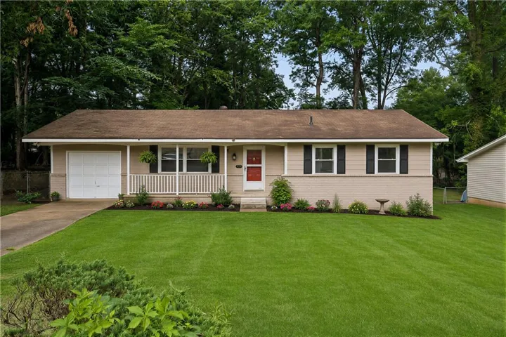 Ranch-style residence featuring a one-car garage, covered front porch, and a red front door