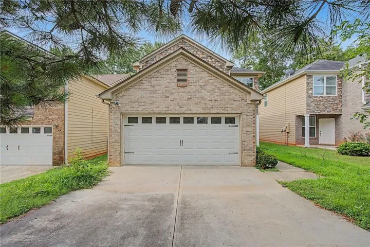 Brick facade home featuring a two-car garage with panel windows and decorative hardware, a gabled roofline, and a concrete driveway
