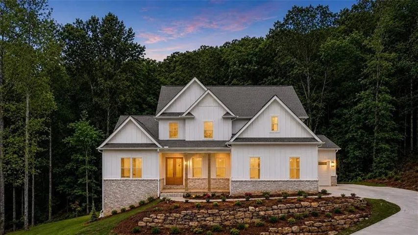 Two-story residence featuring white board and batten siding, stone facade accents, and a dark shingle roof