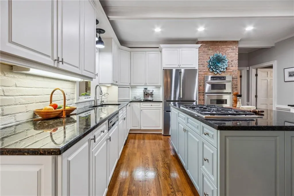 Kitchen with white cabinets, trash compactor, double ovens and exposed brick accent