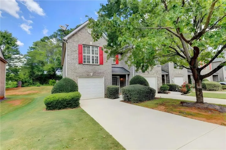 Brick exterior featuring red window shutters, a front entry, and an attached garage
