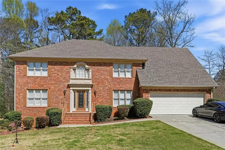 Colonial-style house featuring a front yard, a garage, concrete driveway, and brick siding