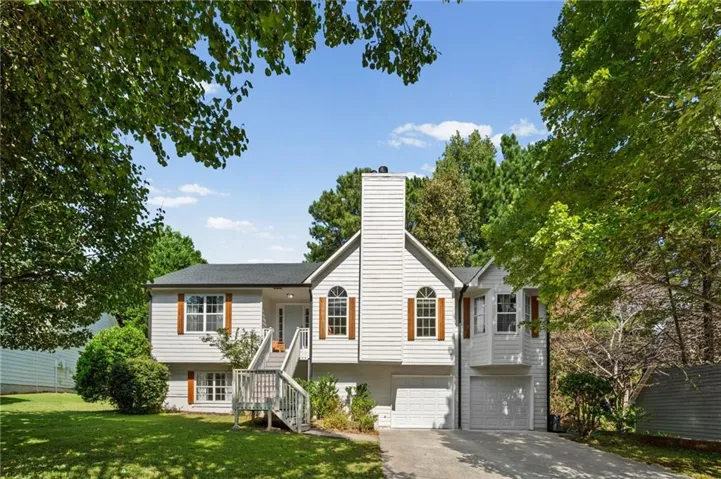 Split-level residence featuring white siding, a prominent chimney, and a multi-level deck