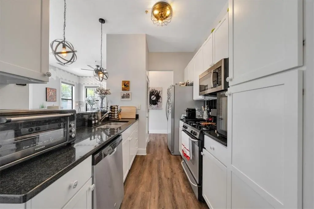 Kitchen featuring white cabinetry, decorative light fixtures, appliances with stainless steel finishes, sink, and dark hardwood / wood-style flooring