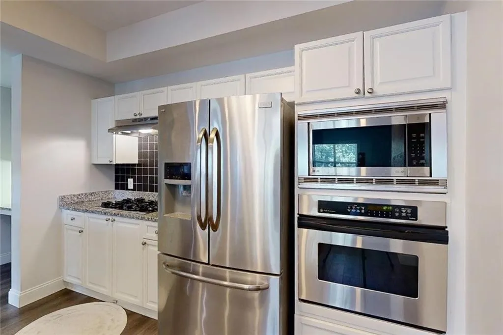 Kitchen featuring appliances with stainless steel finishes, dark wood-style flooring, backsplash, under cabinet range hood, and white cabinetry