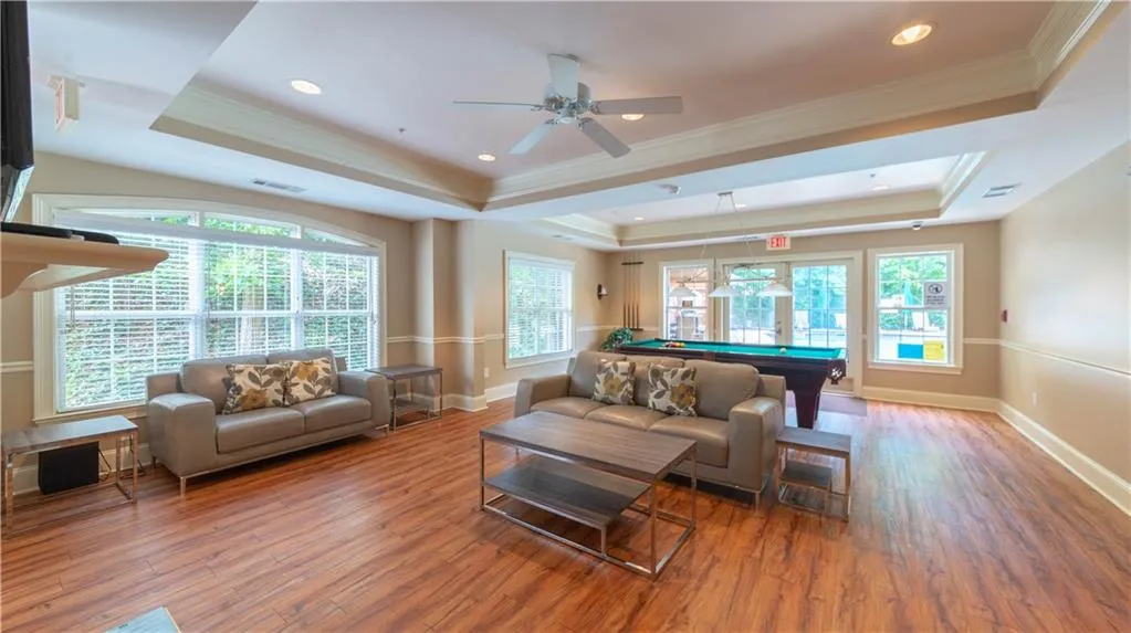 Living area with a raised ceiling, wood finished floors, billiards, healthy amount of natural light, and ornamental molding