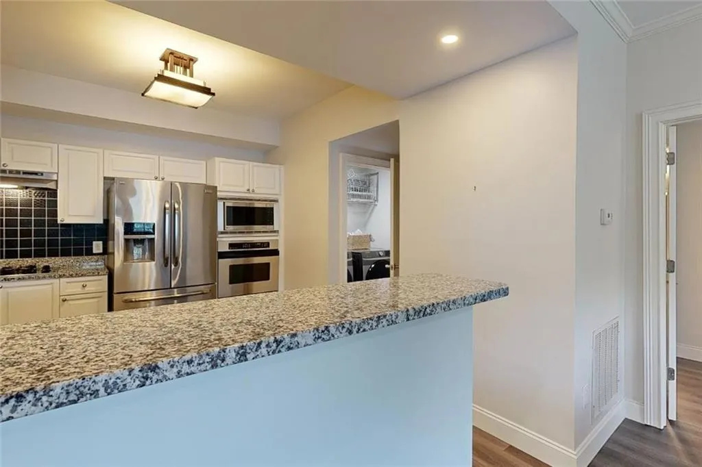 Kitchen with appliances with stainless steel finishes, under cabinet range hood, dark wood finished floors, tasteful backsplash, and independent washer and dryer