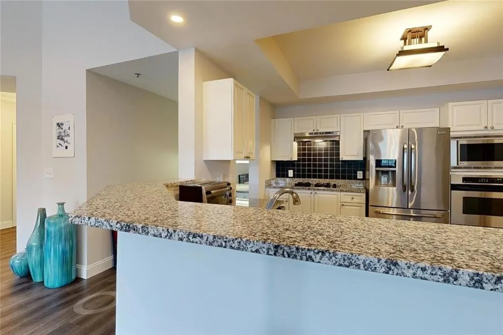 Kitchen featuring stainless steel appliances, dark wood-type flooring, under cabinet range hood, backsplash, and white cabinetry
