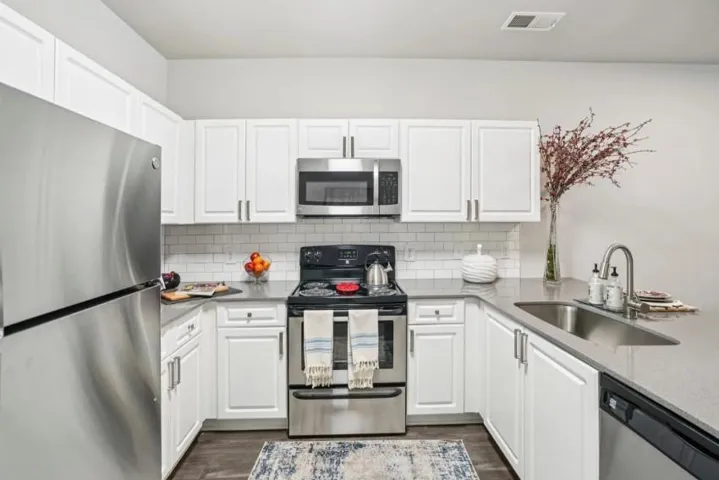 Kitchen with stainless steel appliances, white cabinetry, light stone counters, dark wood-type flooring, and backsplash