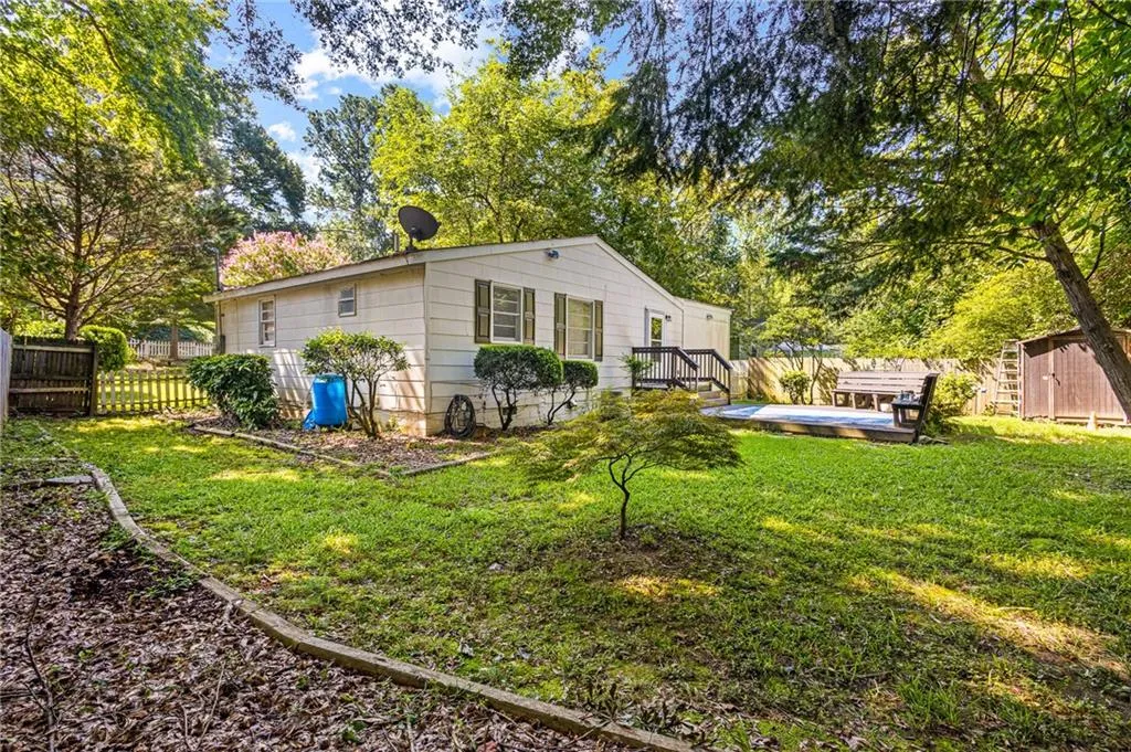View of side of home featuring a wooden deck, a fenced backyard, a storage unit, and view of wooded area