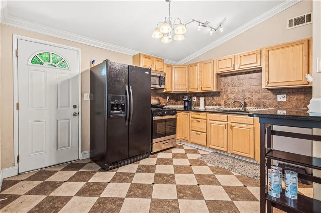 Kitchen with vaulted ceiling, light brown cabinetry, appliances with stainless steel finishes, dark countertops, and crown molding