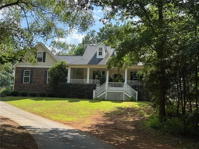 Traditional-style residence featuring a prominent covered front porch with white railings, a partial stone facade, and dormer windows