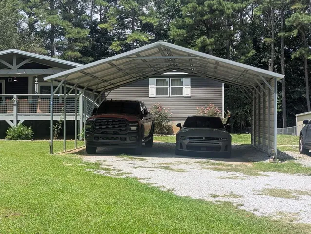 Two-car metal carport with a gravel driveway, front house elevation with vinyl siding, and a wooden deck with metal railing