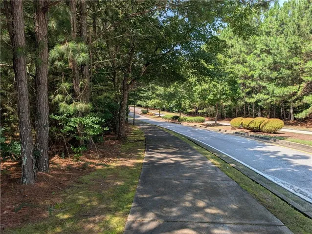 Paved sidewalk bordered by mature trees and a manicured lawn, adjacent to a paved roadway