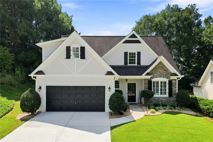 Stone and stucco exterior with dark shutters, an attached two-car garage, and a concrete driveway