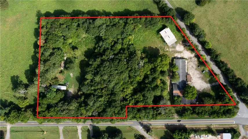 Expansive wooded acreage with visible road frontage, featuring multiple structures including a commercial building with a paved lot