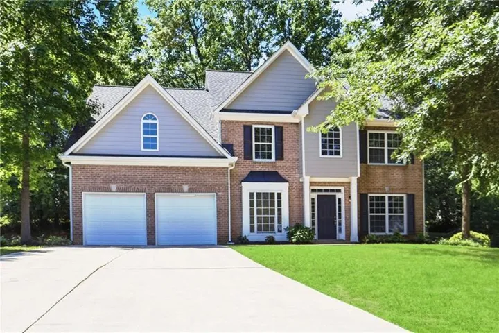 Two-story brick and siding residence featuring a two-car garage, bay window, and a prominent arched window on the upper gable