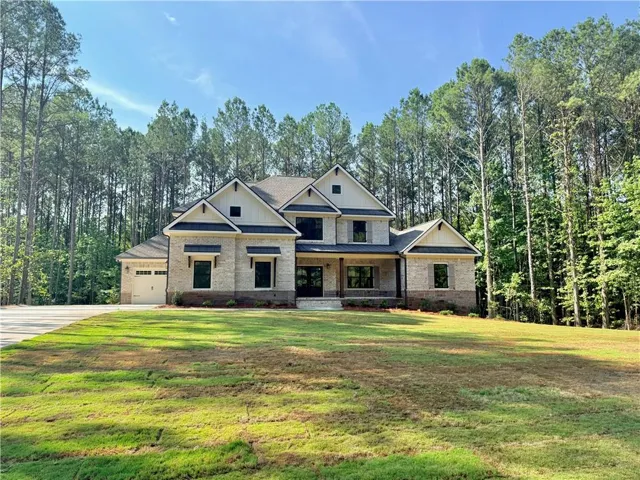 Contemporary two-story residence featuring light brick masonry, a covered porch with column supports, a gabled roofline, a two-car garage, and a lush green lawn