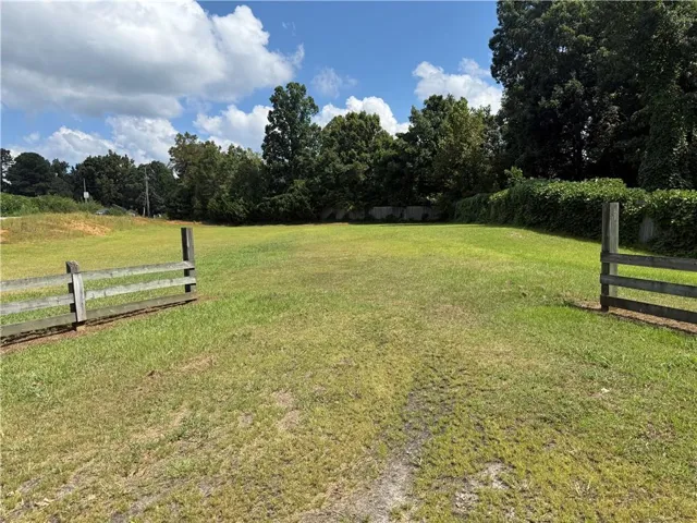 Expansive grassy lot with perimeter fencing and mature trees