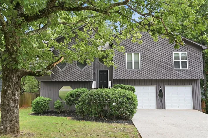 Exterior featuring gray horizontal siding, a dark front entry door, two white garage doors, and unique geometric windows