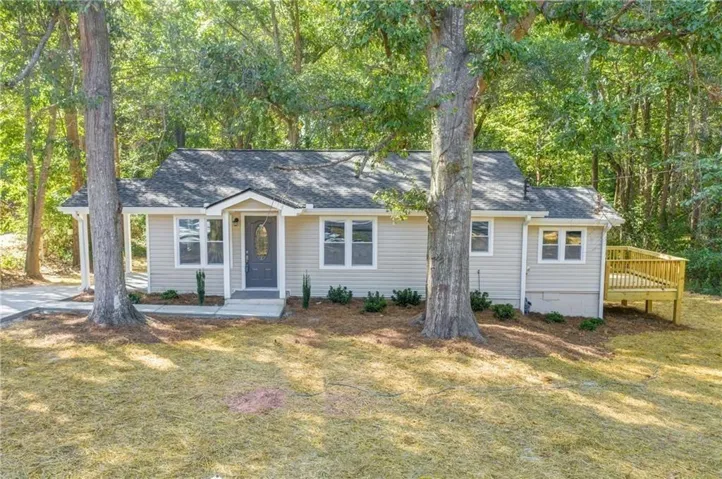 Ranch-style exterior with light-colored siding, a dark gray front door, a front porch, a wood deck, and a shingle roof