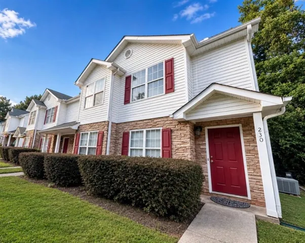 Two-story residential building featuring white siding and stone veneer, dark red entry door, white trim, and red window shutters
