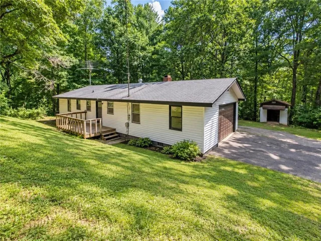 Single-story residence featuring white siding, an attached garage with a dark wood-finish door, and a shingled roof