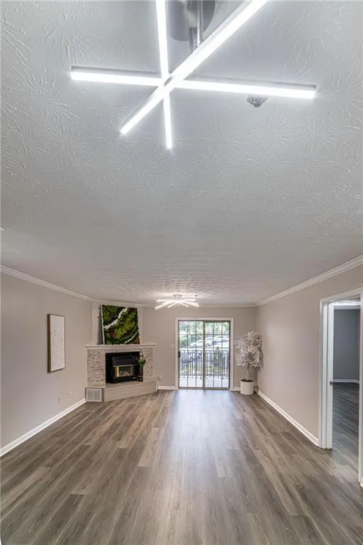 Unfurnished living room featuring dark wood-type flooring, ornamental molding, a fireplace, and a textured ceiling