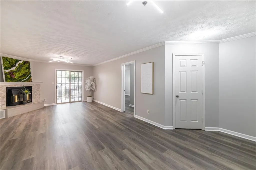 Unfurnished living room with ornamental molding, a textured ceiling, dark wood-style floors, and a glass covered fireplace