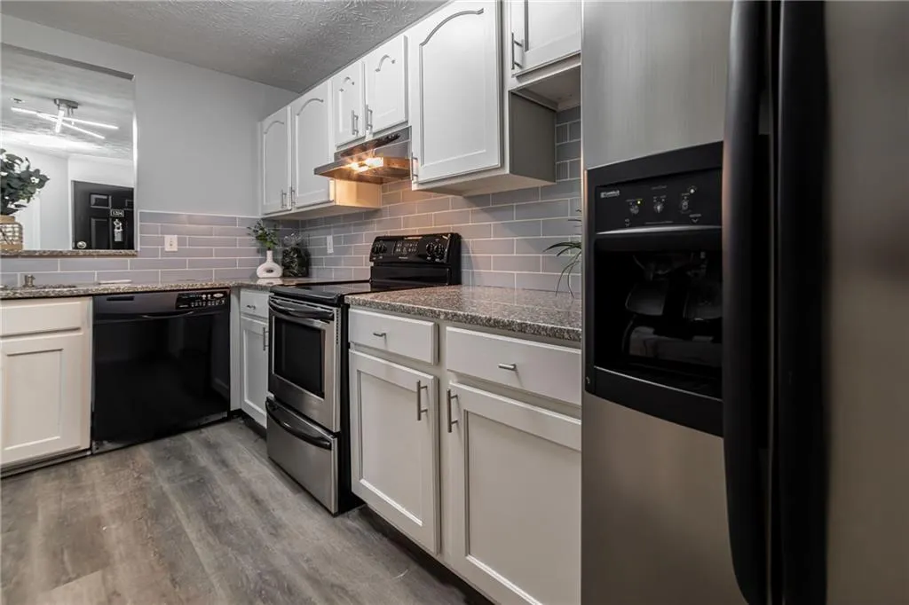Kitchen with appliances with stainless steel finishes, decorative backsplash, dark wood finished floors, under cabinet range hood, and white cabinets