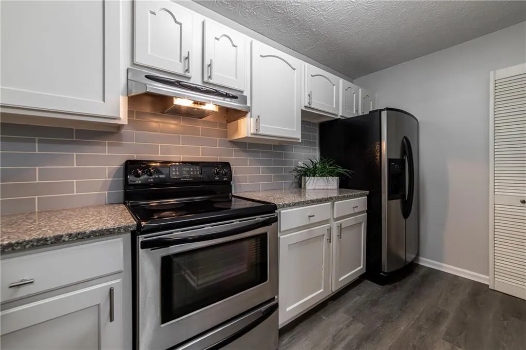 Kitchen featuring stainless steel appliances, under cabinet range hood, dark wood-style flooring, white cabinetry, and a textured ceiling
