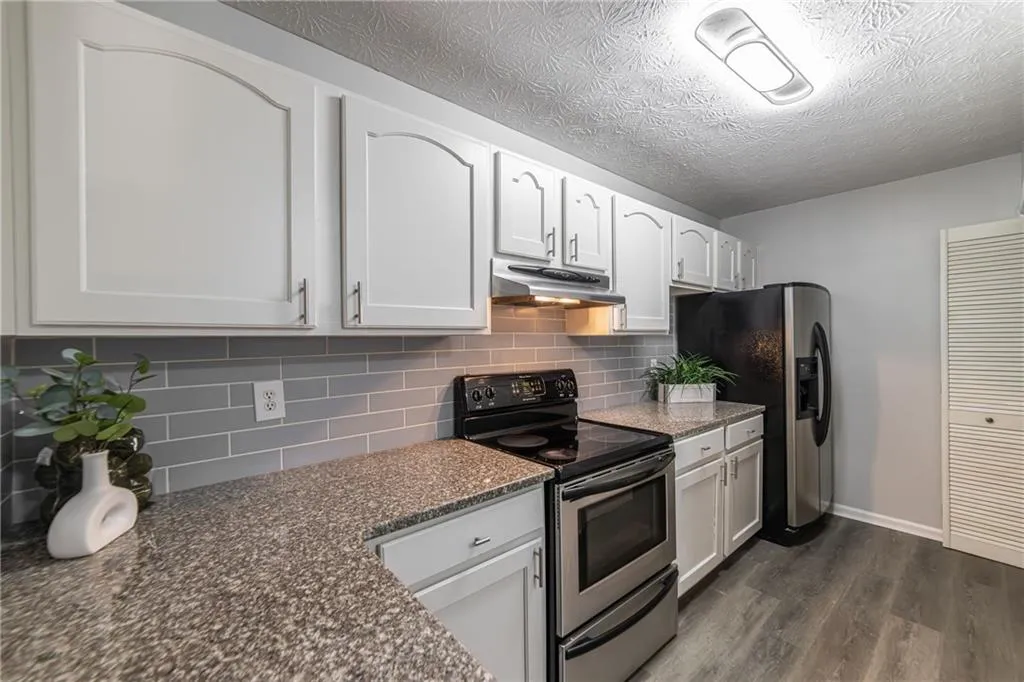 Kitchen featuring appliances with stainless steel finishes, dark wood finished floors, white cabinetry, decorative backsplash, and under cabinet range hood