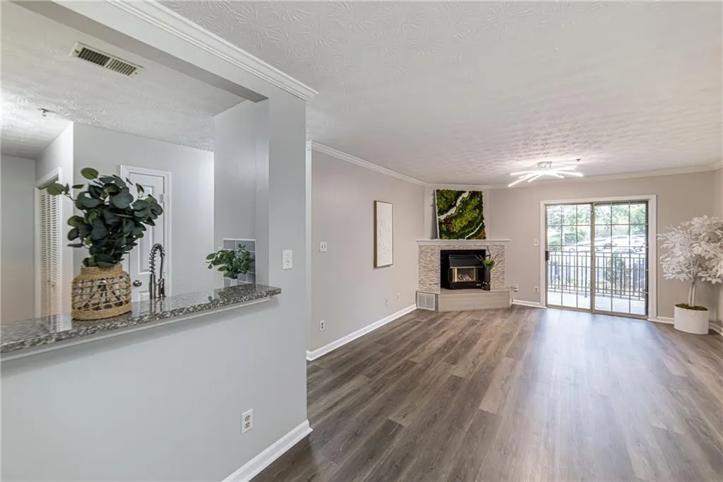 Unfurnished living room featuring wood finished floors, a stone fireplace, a textured ceiling, and ornamental molding