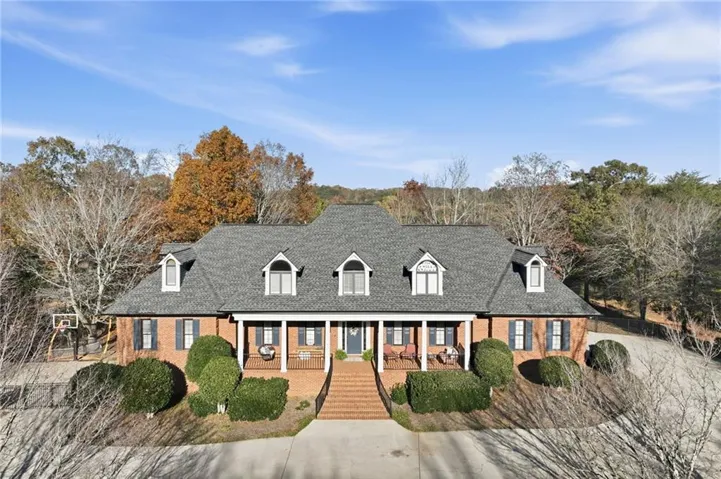 Cape cod house with brick siding, covered porch, roof with shingles, and stairway