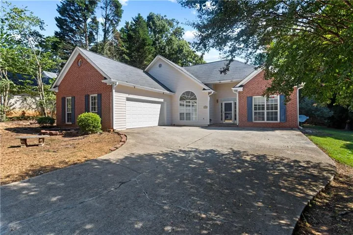 Brick and siding exterior with a concrete driveway, attached garage, and mature landscaping