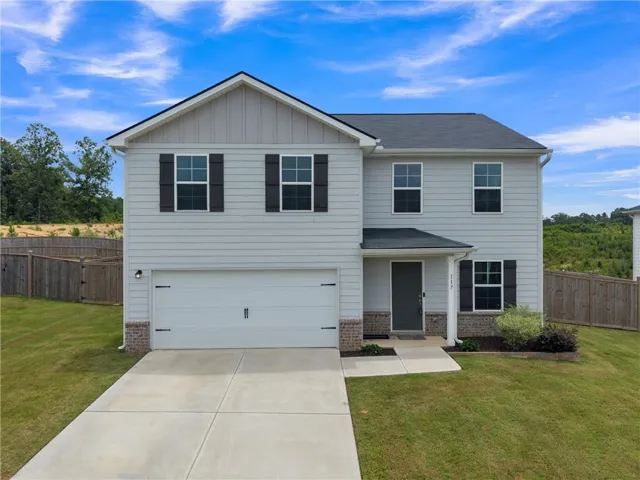 Two-story residence featuring light gray siding with dark shutters, an attached two-car garage, a dark front door, and a concrete driveway