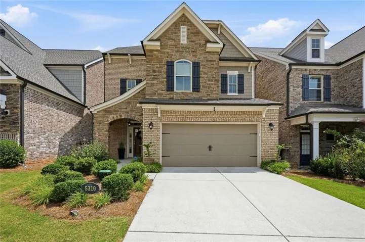 Stone and brick facade featuring a two-car garage, arched entryway, and mature landscaping