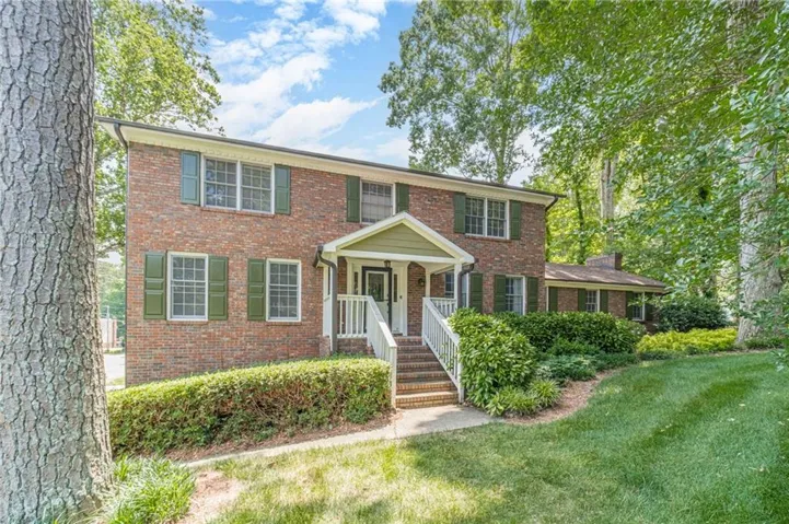 Brick exterior featuring green shutters, a covered front entry, and a prominent front porch with white railings