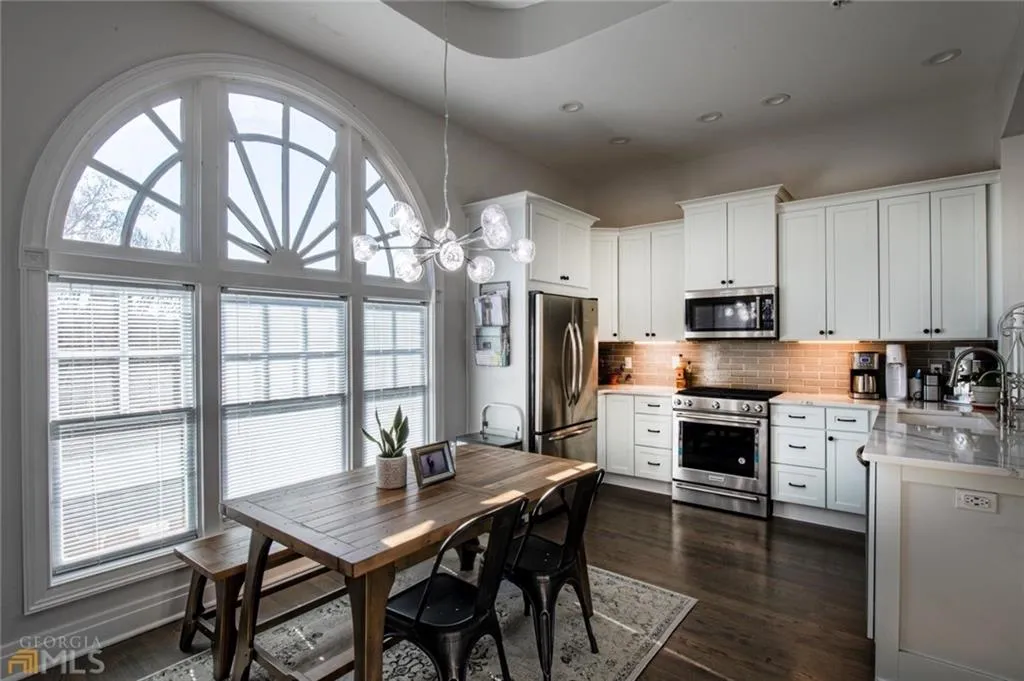Kitchen with stainless steel appliances, light stone countertops, white cabinetry, backsplash, and hanging light fixtures