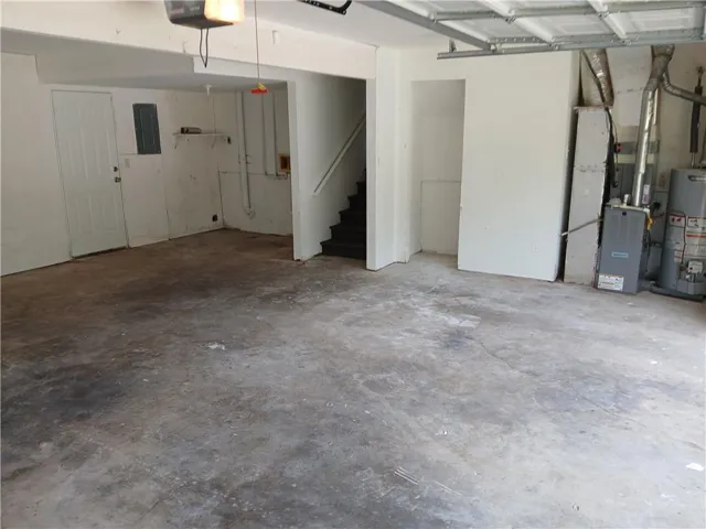 Spacious garage featuring a concrete floor, overhead garage door system, interior access door, utility access panel, and staircase